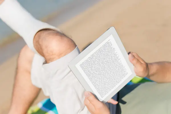 Jemand liegt mit einem Bein im Gips am Strand und liest ein Buch.