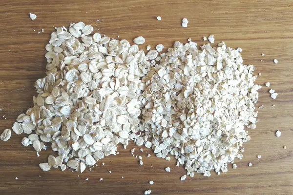Grobe und feine Haferflocken liegen nebeneinander auf einem Holztisch.