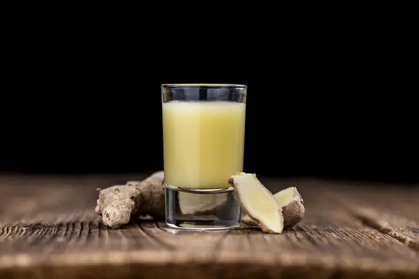Ein Glas mit einem Ingwershot steht auf dem Tisch, daneben liegen Ingwerwurzeln.