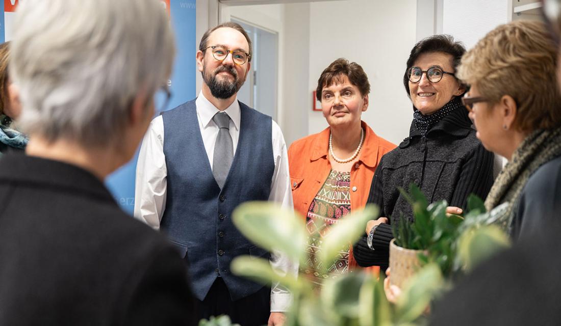 Drei Personen stehen im Raum und lächeln in die Kamera.