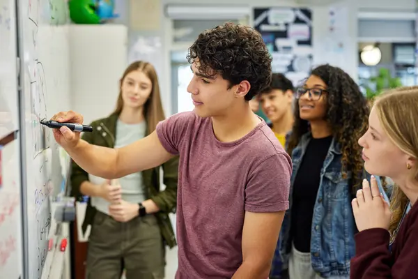 Schüler schreibt etwas auf ein Whiteboard und andere Schüler schauen zu