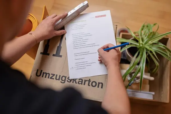 Mann schreibt Liste auf Umzugskarton