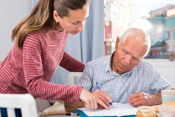 Eine Frau hilft einem Senior beim Ausfüllen von Dokumenten an einem Frühstückstisch