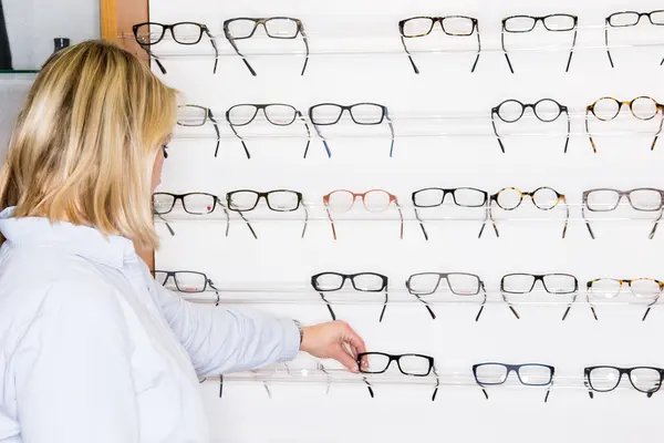 Eine Frau steht beim Optiker vor einer großen Auswahl an Brillen.