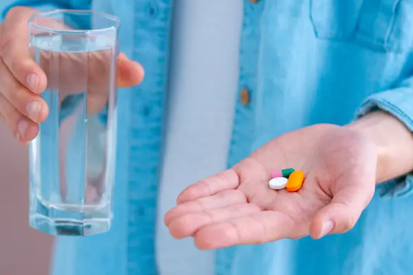 Jemand hält Tabletten in einer Hand und in der anderen ein Glas Wasser.