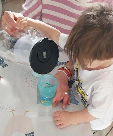 Ein Kind wird beim Eingießen von Wasser unterstützt