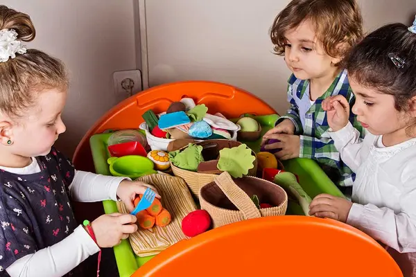 Kita-Kinder sitzen an einem Tisch und bereiten mit Spielzeug-Gemüse essen zu