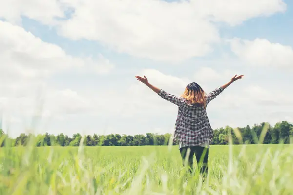 Eine junge Frau steht mit offenen Armen auf einem Feld.
