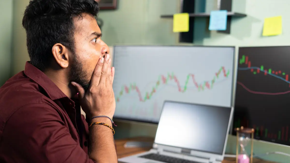 Mensch sitzt vor Computerbildschirmen mit Trading-Kurven und ist schockiert