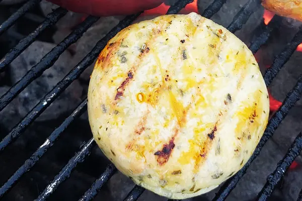 Ein runder, gegrillter Käse liegt auf einem Grillrost.