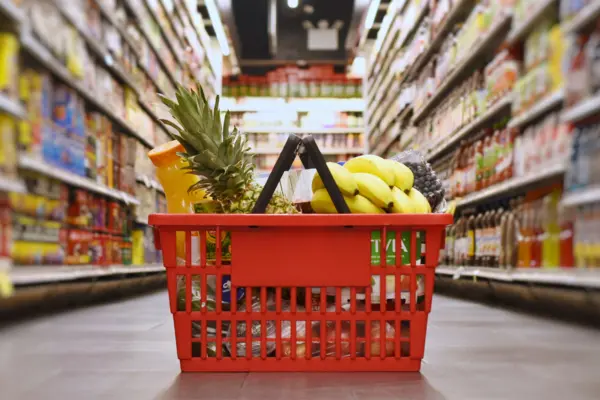 Ein gefüllter Einkaufskorb steht im Gang eines Supermarktes. 