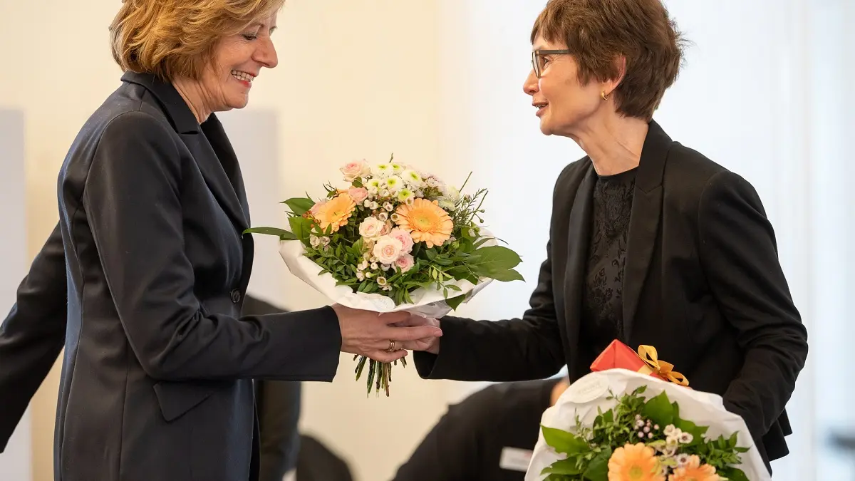 Zwei Frauen auf einer Bühne. Die eine überreicht der anderen einen Blumenstrauß.