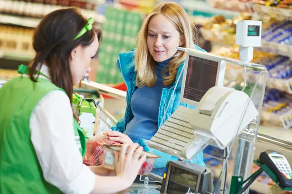Eine Frau steht in einem Supermarkt an einer Kasse und kauft ein.