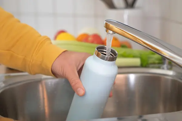 Jemand füllt am Wasserhahn seine Trinkflasche auf