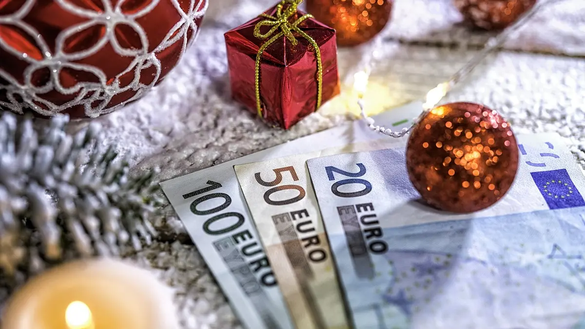 Eine Christbaumkugel liegt auf Euro-Scheinen um Weihnachtsgeld darzustellen