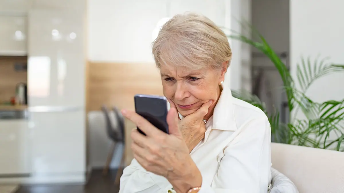 Eine ältere Frau schaut kritisch auf ihr Smartphone