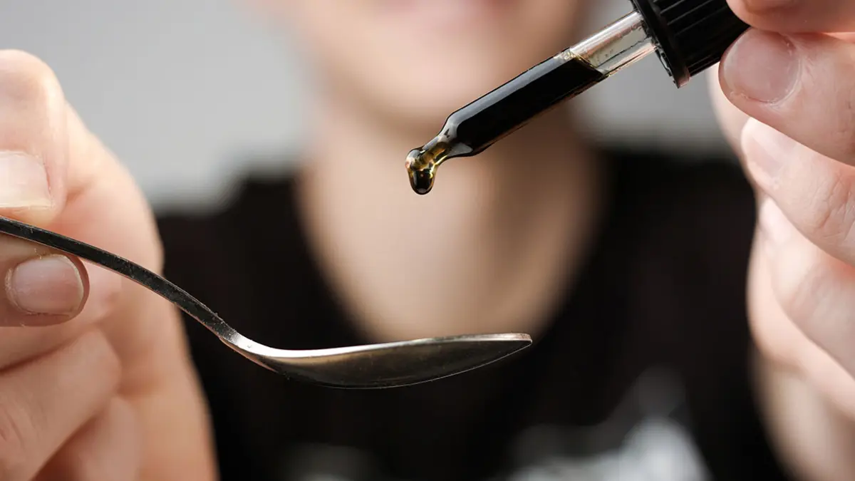 Jemand träufelt aus einer Pipette eine dunkle Flüssigkeit auf einen Löffel