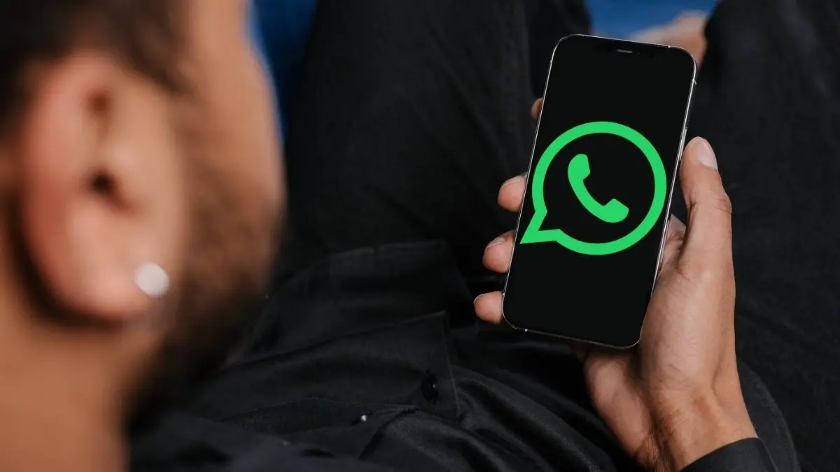 Mann mit Smartphone in der Hand, auf dessen Display das grüne Logo von WhatsApp zu sehen ist.