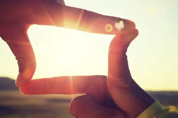Bild mit Händen, die die Sonne einrahmen.