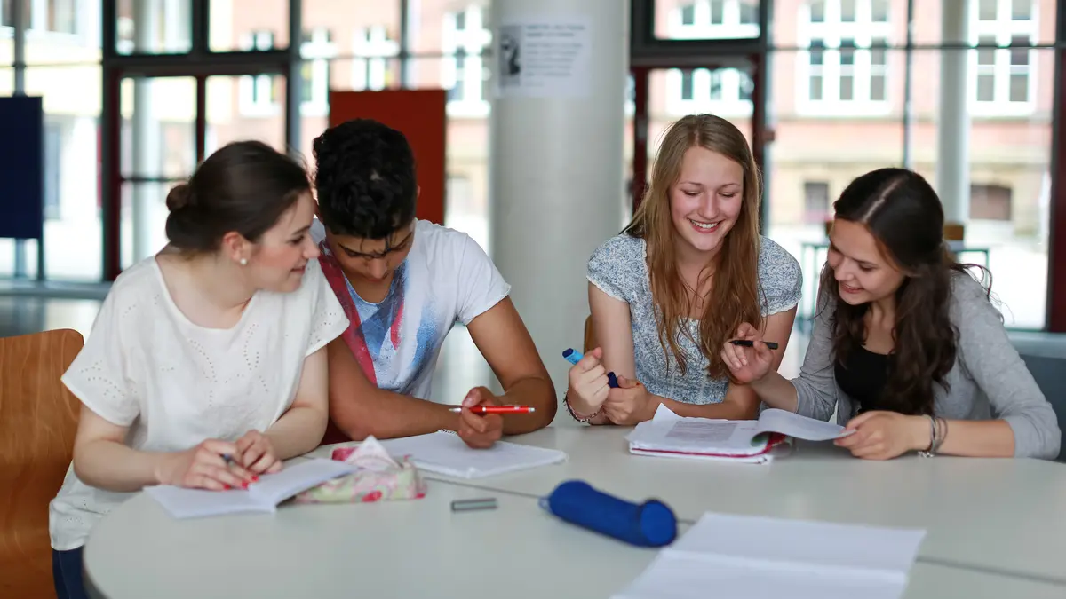 Vier Schüler*innen sitzen an einem Tisch und lernen gemeinsam
