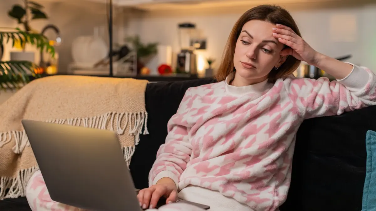 Frau sitzt auf dem Sofa und schaut kritisch auf einen Laptopbildschirm