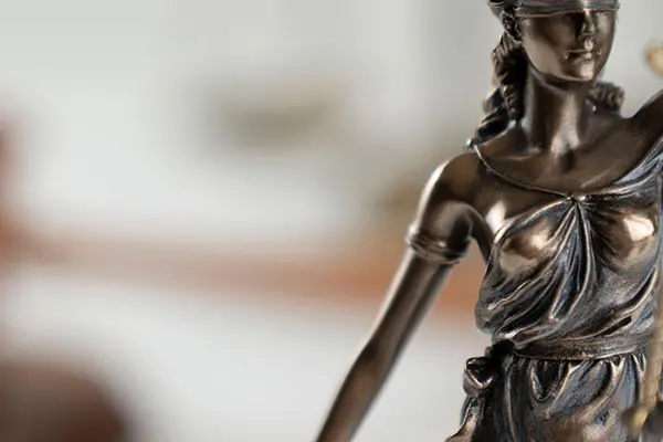 Eine Skulptur der Justitia auf einem Tisch, im Hintergrund der Hammer des Gerichts