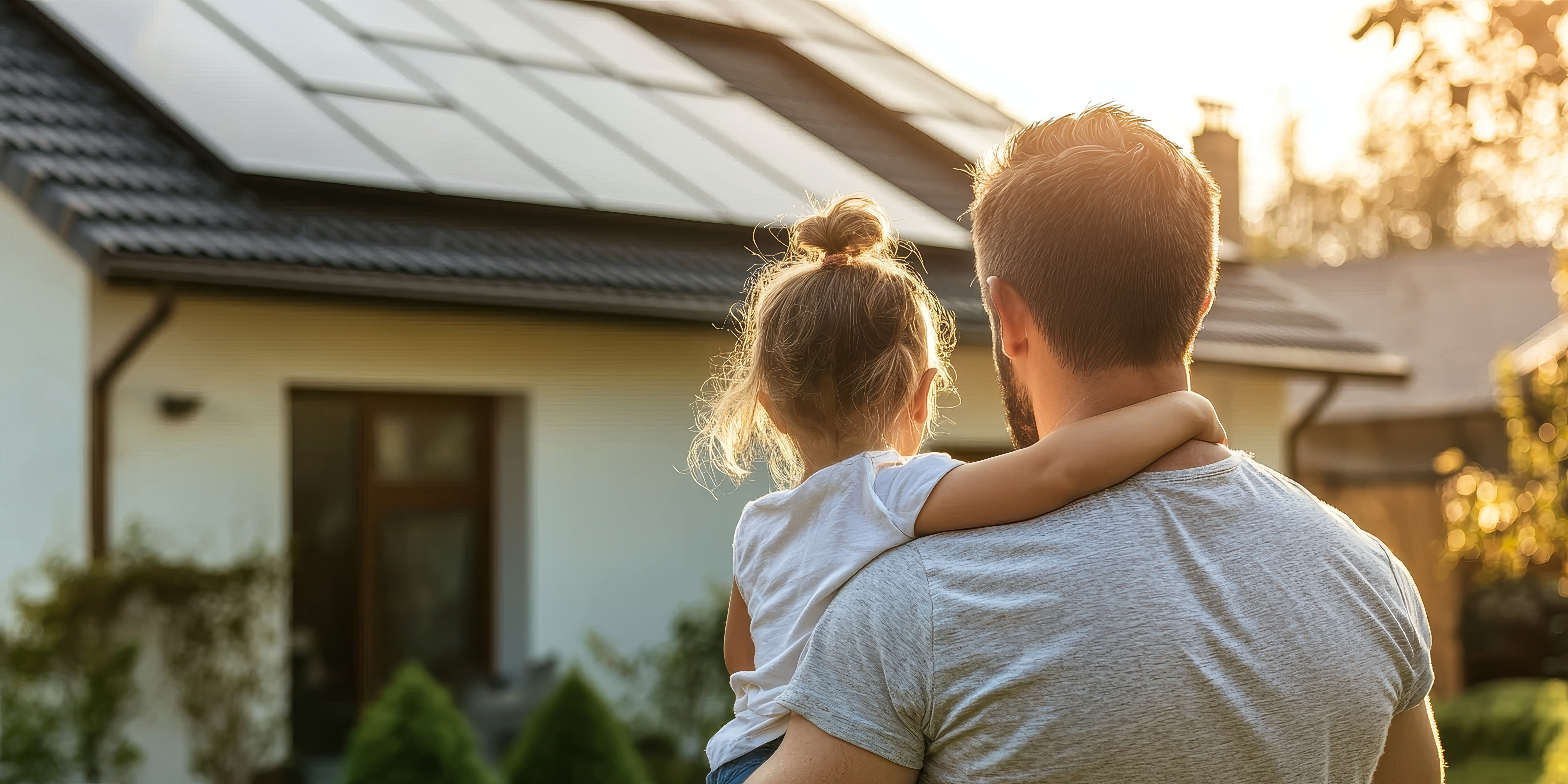 Mann mit Kind blickt auf Photovoltaikanlage auf dem Dach des Eigenheims