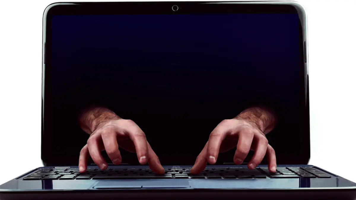 Hände greifen aus einem Laptop-Bildschirm heraus auf die Tastatur davor