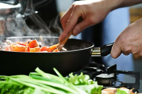 Pfanne mit dampfendem Gemüse, Hand hält Kochlöffel, Nahaufnahme