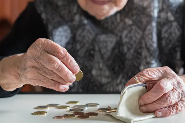Eine ältere Dame zählt Bargeld, das vor ihr auf dem Tisch liegt