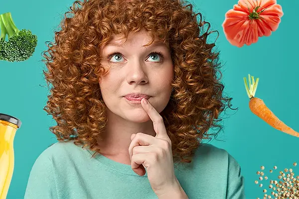 Eine junge Frau mit roten Locken blickt nachdenklich nach oben, um sie herum sind verschiedene gesunde Lebensmittel angeordnet 