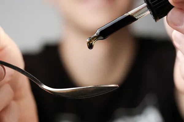 Jemand träufelt aus einer Pipette eine dunkle Flüssigkeit auf einen Löffel