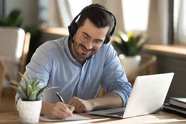 Videoberatung: Ein Mann sitzt mit Laptop und Headset an einem Tisch und macht Notizen