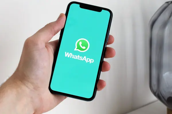 Eine Hand hält ein Smartphone, dessen Display das Logo von WhatsApp und die Schrift "WhatsApp" zeigt.