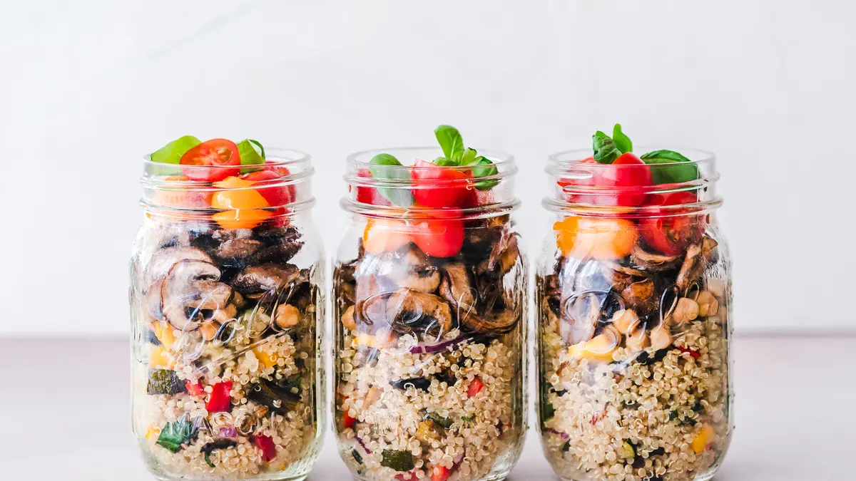 3 große Einmachgläser, welche jeweils mit Quinoa Salat (unterste Schicht), gebratenen Pilzen (mittlere Schicht) und halbierten Cherry-Tomaten und Basilikum (oberste Schicht) befüllt sind.