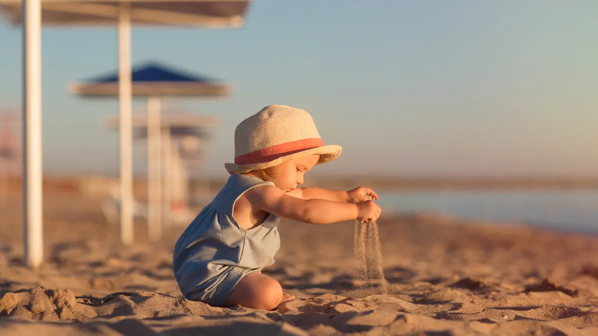 Ein Kind spielt am Strand im Sand und trägt einen Hut gegen die Sonne