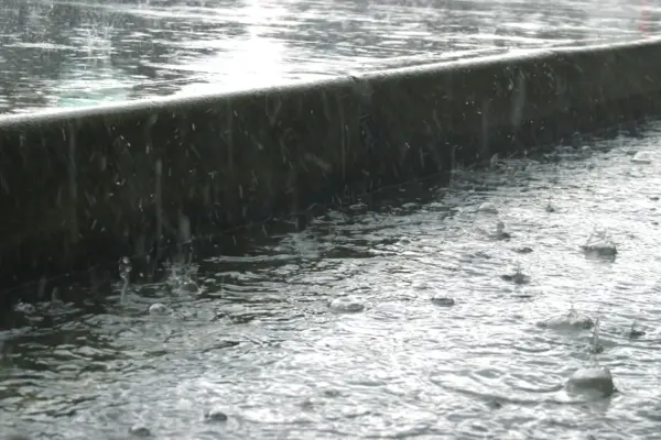 starker Regen fällt auf einen Gehweg, vor dem Bordstein sammelt sich das Wasser