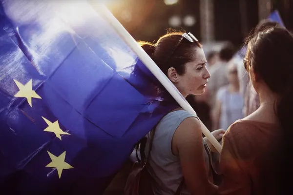  Zwei Personen stehen zusammen; eine von ihnen hält eine große EU-Flagge in der Hand