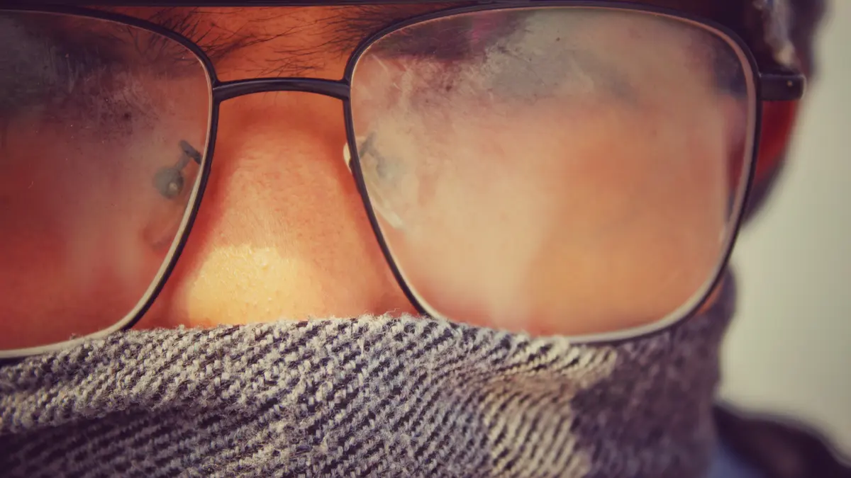 Ein Mann mit Schal um den Mund trägt eine Brille mit beschlagenen Gläsern