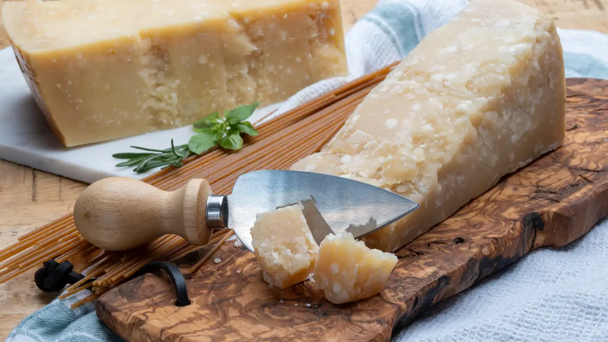 Zwei Stück Parmesan liegen auf zwei Brettern. Das vordere Stück ist mit einem Käsemesser angeschnitten.