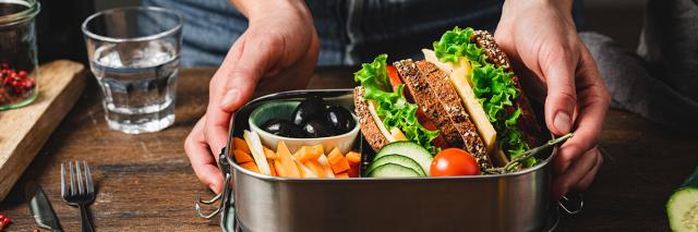 Jemand bereitet eine Lunchbox mit Broten, Obst und Gemüse zu