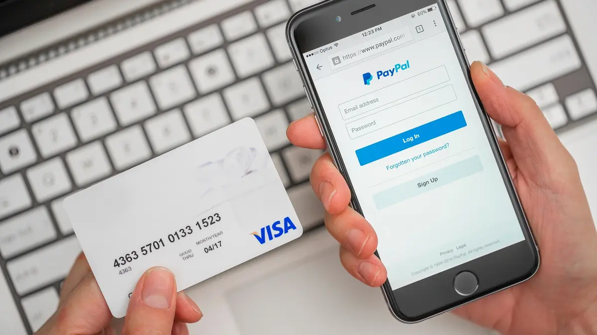 Auf einem Handy wird der Paypal-Login Screen angezeigt. Daneben sieht man eine Kreditkarte