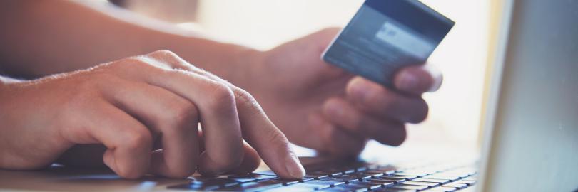 eine rechte Hand macht Eingaben auf einem Laptop, die linke hält eine Kreditkarte