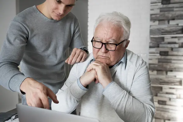 Schmuckbild: Älterer und jüngerer Mann schauen gemeinsam auf Laptop
