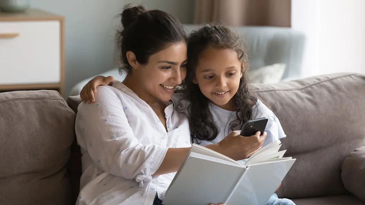 Mutter und Kind sitzen gemeinsam auf der Couch und schauen auf einen Smartphone.