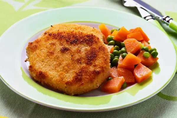 Sellerieschnitzel mit Erbsen und Möhren auf einem Teller.