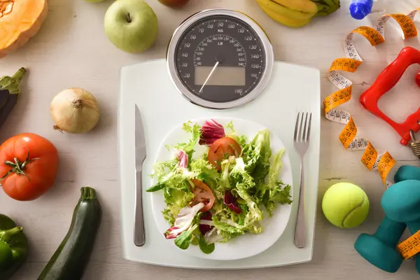 Auf einer Körperwaage steht ein Teller mit Salat, links und rechts daneben liegen Messer und Gabel.