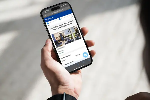 Smartphone in einer Hand, auf dem Display ist eine Internetseite zu sehen, die booking.com ähnelt.