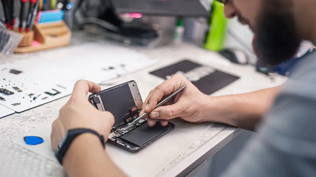 Ein Mann repariert ein Smartphone an einem Werkstatttisch.