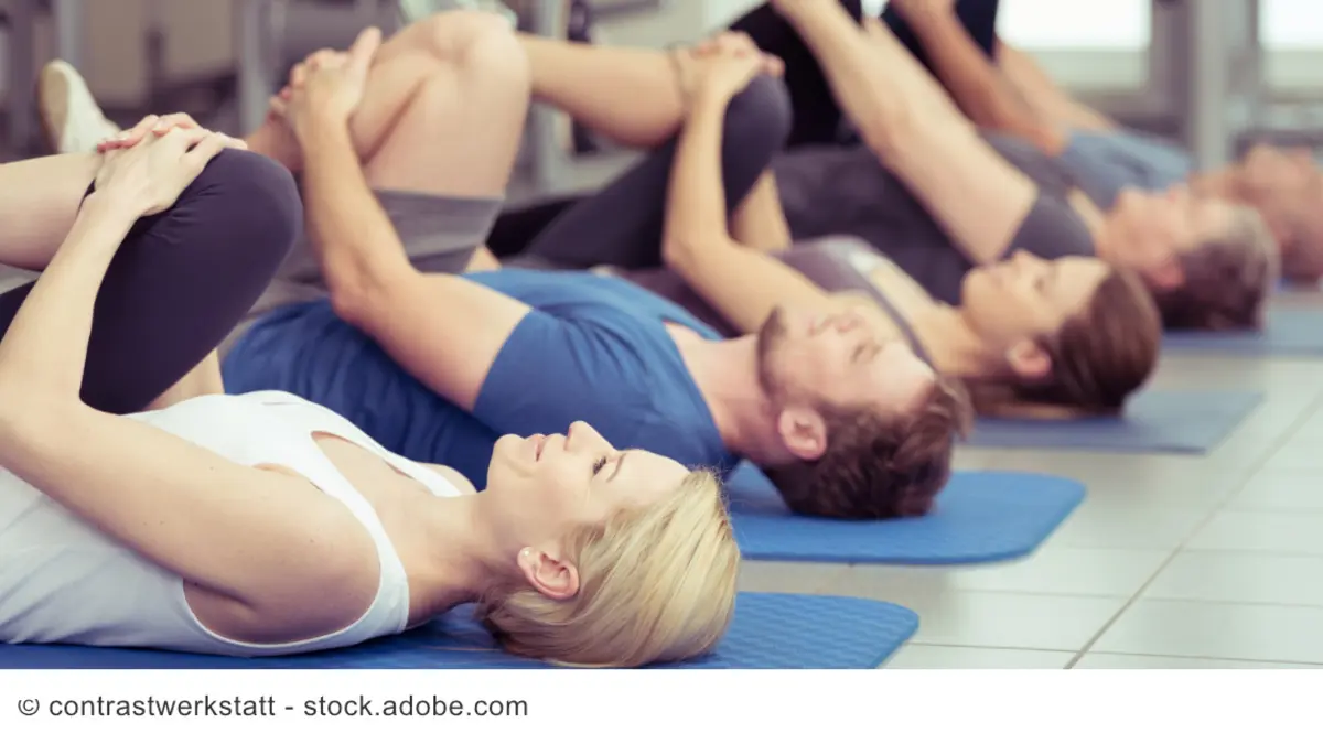 Eine Gruppe Menschen liegt bei einem Sportkurs auf Trainingsmatten.